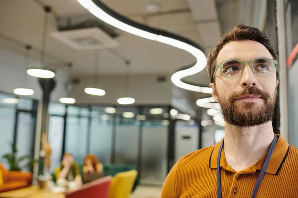Professional headshot of bearded businessman in eyeglasses near blurred coworkers talking in office — Stock Photo