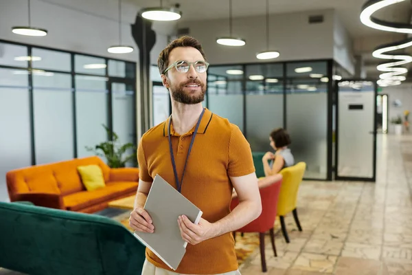 Smiling bearded businessman in eyeglasses, with documents near blurred colleague in coworking office — Stock Photo