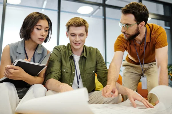 Bearded entrepreneur pointing at blueprint near young architects, teamwork and productivity — Stock Photo