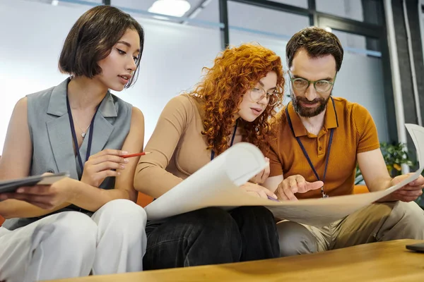 Bearded entrepreneur and young businesswomen pointing at blueprint, teamwork, startup project — Stock Photo