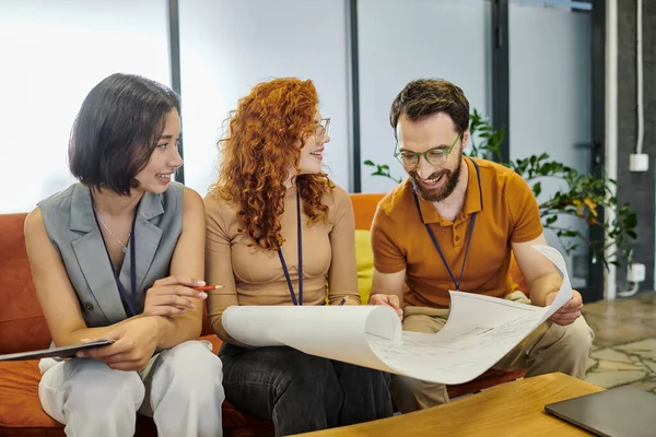 Imprenditore barbuto sorridente guardando cianografia vicino giovane donna d'affari, lavoro di squadra di successo — Foto stock