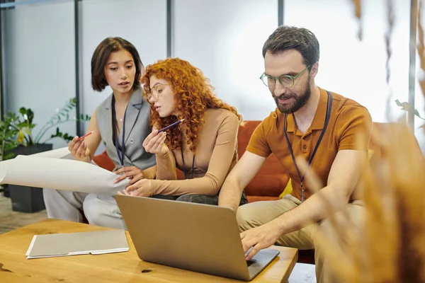 Bearded businessman working on laptop, young architects with blueprint and pencils, startup project — Stock Photo