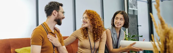 Smiling redhead architect talking to pleased businessman near woman with blueprint in office, banner — Stock Photo
