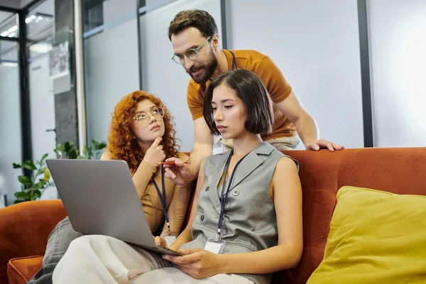 Bearded team lead pointing at laptop near young women planning startup project in coworking office — Stock Photo