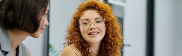 Redhead businesswoman in eyeglasses talking to colleague in contemporary office, banner — Stock Photo