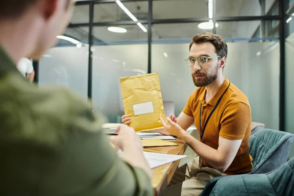 Bearded businessman showing envelope to blurred colleague, modern office, workplace — Stock Photo