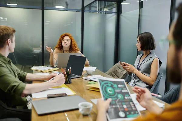 Redhead-Team führt Gespräche mit Kollegen in der Nähe von Laptops und Dokumenten im Besprechungsraum, Startup-Projekt — Stockfoto