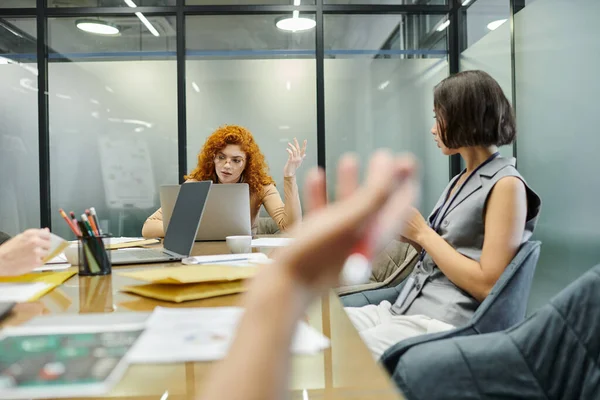 Meeting room, laptops, documents, redhead team lead and colleagues discussing business project — Stock Photo