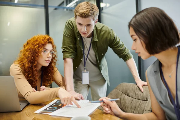 Redhead businesswoman pointing at graphs near team lead and colleague in office, startup project — Stock Photo