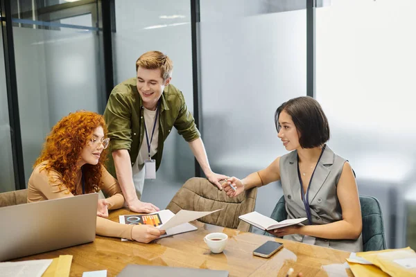 Redhead businesswoman with document near laptop and colleagues in meeting room, creative teamwork — Stock Photo