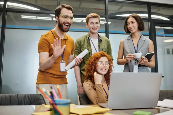 Joyeux entrepreneur barbu agitant la main lors de la vidéoconférence près des partenaires d'affaires au bureau — Photo de stock
