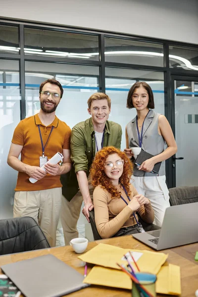 Creative team looking at camera near laptop in office, professional headshot, business success — Stock Photo