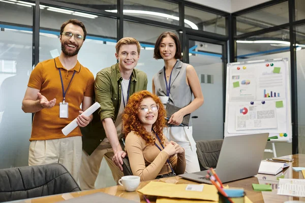 Счастливая бизнес-команда смотрит на камеру рядом с ноутбуком в офисе, профессиональный хедшот, успех — стоковое фото