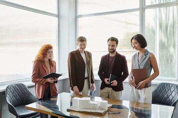 Positive investors and young architects looking at building model during meeting in office — Stock Photo