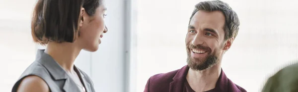 Радісний бородатий підприємець посміхається біля молодої бізнес-леді в сучасному офісі, банер — стокове фото