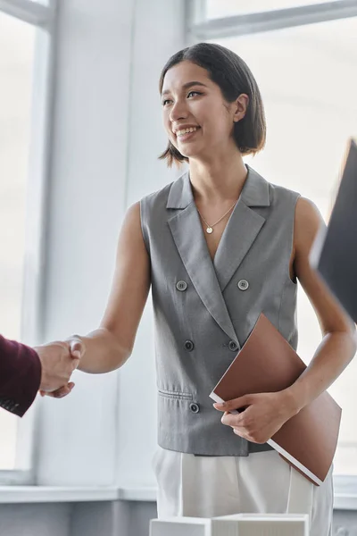 Donna d'affari felice con cartella che stringe la mano con compagno d'affari in ufficio, collaborazione — Foto stock