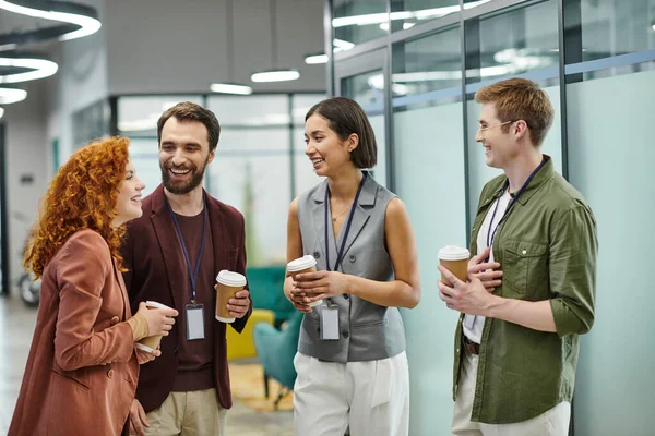 Gerentes sonrientes sosteniendo café para ir durante la conversación en la moderna oficina de coworking - foto de stock