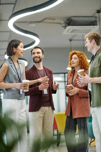 Jovem empresária conversando com colegas alegres com copos de papel, coffee break no escritório moderno — Fotografia de Stock