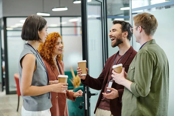 Heureux homme d'affaires barbu riant près de collègues avec des tasses jetables, pause café dans le bureau — Photo de stock