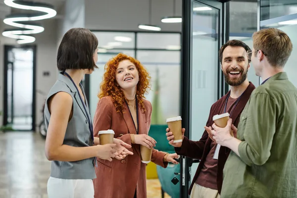 Successful business team with paper cups smiling and talking during coffee break in office — Stock Photo