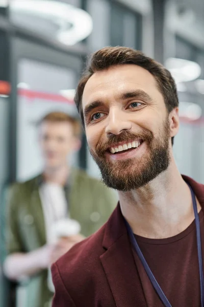 Веселый бородатый бизнесмен смотрит в сторону коллеги на размытом фоне в коворкинг-офисе — стоковое фото