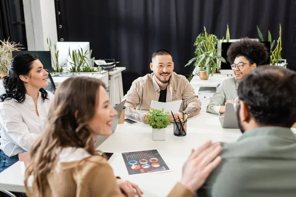 Happy multicultural business people discussing project and brainstorming near team lead in office — Stock Photo