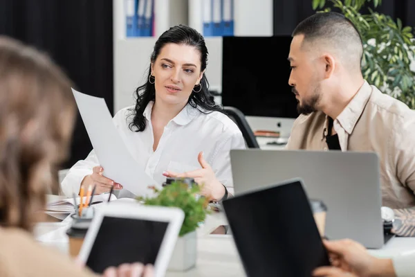 Asian man talking to brunette female colleague while working together in office, sharing ideas — Stock Photo