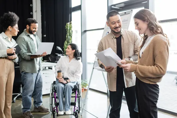 Diversity and inclusion, happy asian man communicating with woman near disabled female coworker — Stock Photo