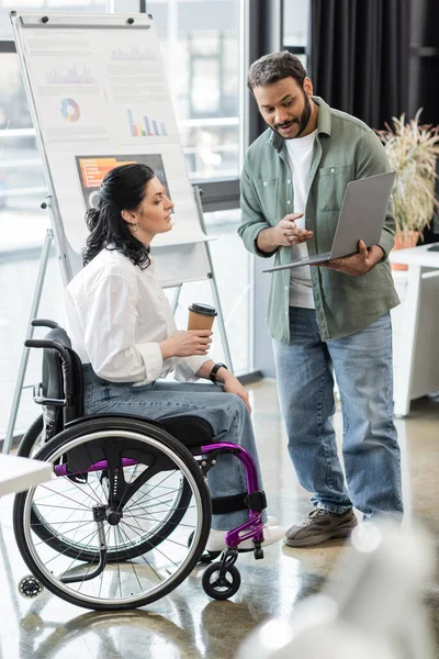 Homme indien montrant le projet de démarrage sur ordinateur portable pour femme handicapée en fauteuil roulant, concept d'inclusion — Photo de stock