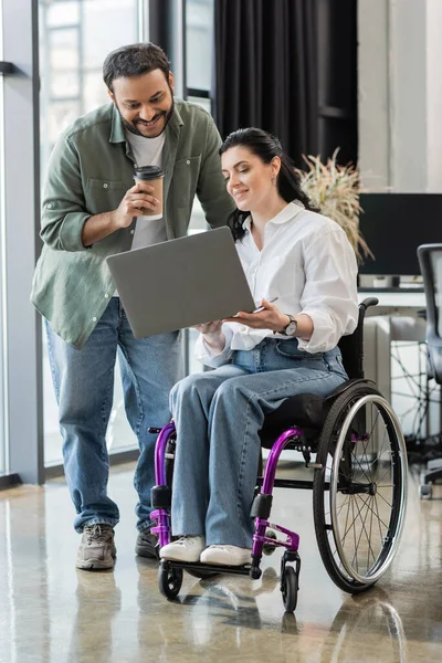 Feliz empresario indio discutiendo proyecto de startup con mujer discapacitada en silla de ruedas, inclusión - foto de stock