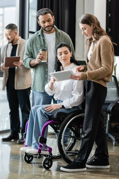 Disabled woman in wheelchair looking at tablet, discussing startup project with interracial team — Stock Photo