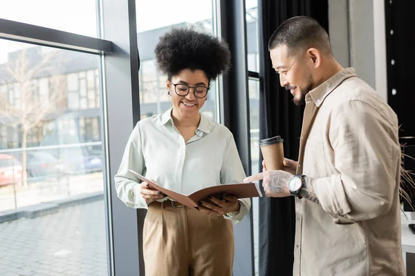 African american woman showing startup project in folder to happy asian businessman in office — Stock Photo