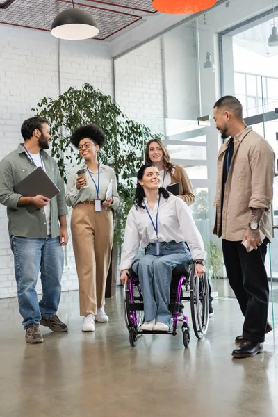 Різноманітність і включення, інвалідність жінки в інвалідному візку дивиться на азіатського колегу поблизу команди — стокове фото