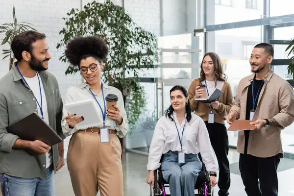 Diversité et inclusion, femme handicapée en fauteuil roulant près de collègues interraciaux avec des étiquettes de nom — Photo de stock