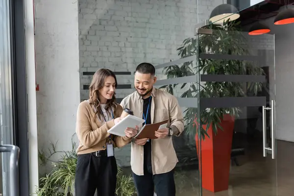 Zufriedene Geschäftsfrau zeigt einem asiatischen Kollegen im modernen Coworking Space Tablet mit Startup-Projekt — Stockfoto
