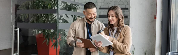 Happy businesswoman showing tablet with startup project to asian colleague in modern office, banner — Stock Photo