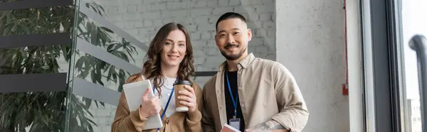 Glückliche Frau mit Pappbecher mit Kaffee und Tablette in der Nähe eines asiatischen Geschäftsmannes in der Pause, Transparent — Stockfoto
