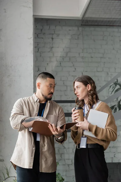 Pretty businesswoman discussing startup project with focused asian colleague holding startup plan — Stock Photo