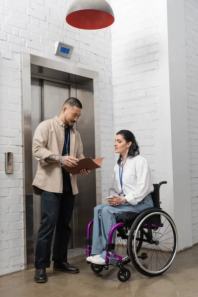 Inclusion and diversity, asian man holding startup plan near disabled woman and office elevators — Stock Photo
