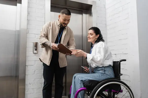 Inclusão e diversidade, asiático homem mostrando startup plano para deficiente mulher perto de escritório elevadores — Fotografia de Stock