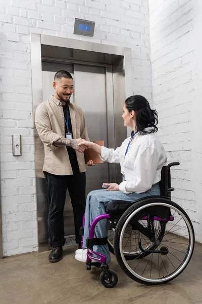 Inclusione e diversità, felice uomo asiatico stringendo la mano con donna disabile vicino ascensori ufficio — Foto stock