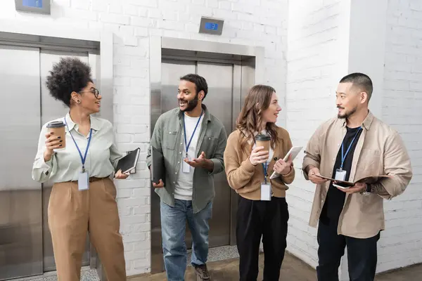 Cultural diversity, happy multicultural creative team with badges chatting near office elevators — Stock Photo