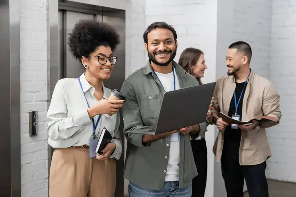 Happy african american woman and indian man looking at camera near office elevators, diversity — Stock Photo