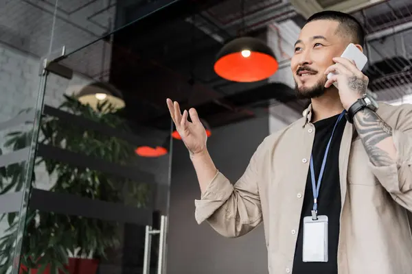 Glücklicher asiatischer Geschäftsmann mit tätowierter Geste beim Telefonieren im modernen Büro — Stockfoto