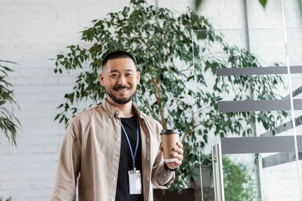 Happy asian businessman with tattoo holding coffee to go and looking at camera, corporate life — Stock Photo
