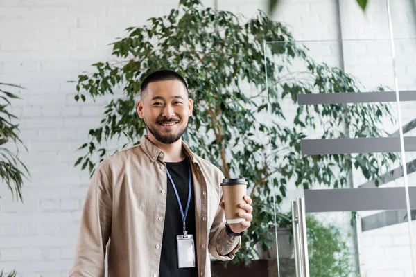 Felice uomo d'affari asiatico con tatuaggio in possesso di caffè per andare e guardando la fotocamera, la vita aziendale — Foto stock