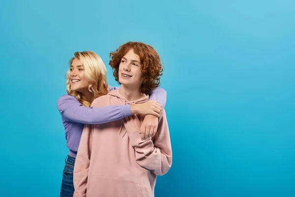 Adolescentes despreocupados com capuzes olhando para o azul, menina loira feliz abraçando adolescente cara, amizade — Fotografia de Stock