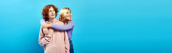 Elegantes amigos adolescentes em capuzes olhando para longe em azul, menina adolescente loira abraçando amigo ruiva — Fotografia de Stock