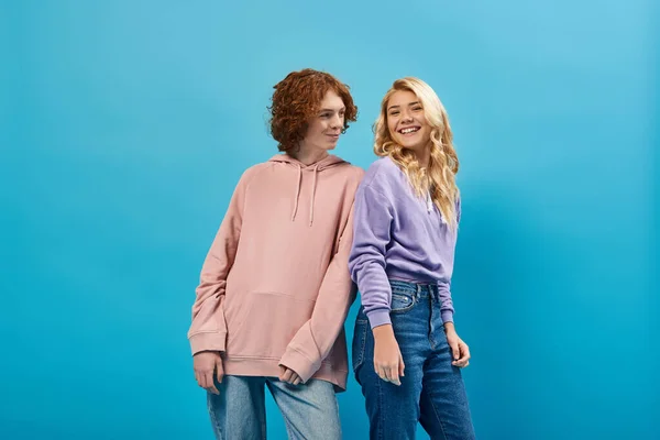 Fröhliche Teenager-Freunde in Kapuzenpullis und Jeans stehen und posieren auf blauen, fröhlichen Emotionen — Stockfoto
