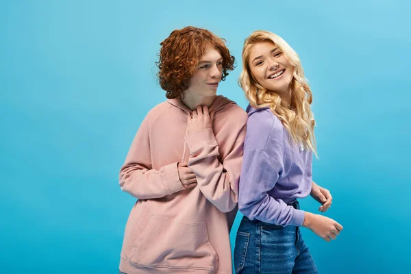 Excited blonde teen girl laughing at camera near smiling redhead boyfriend on blue — Stock Photo